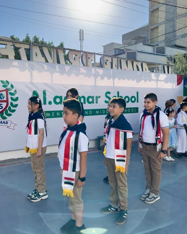 طلبة يشاركون في احتفالية وطنية أمام لافتة المدرسة